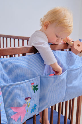 Discover our three-compartment crib organizer pouch, ideal for storing bedtime stories, pacifiers and comforters. Made from OEKO-TEX-certified cotton, it brings a touch of style and refinement to your baby's room, thanks to its cheerfully placed embroidery and bright colors. Its ideal size enables it to fit 120x60cm or 140x70cm cribs. A real decorative touch, it provides a designer storage solution.26 PARADIS